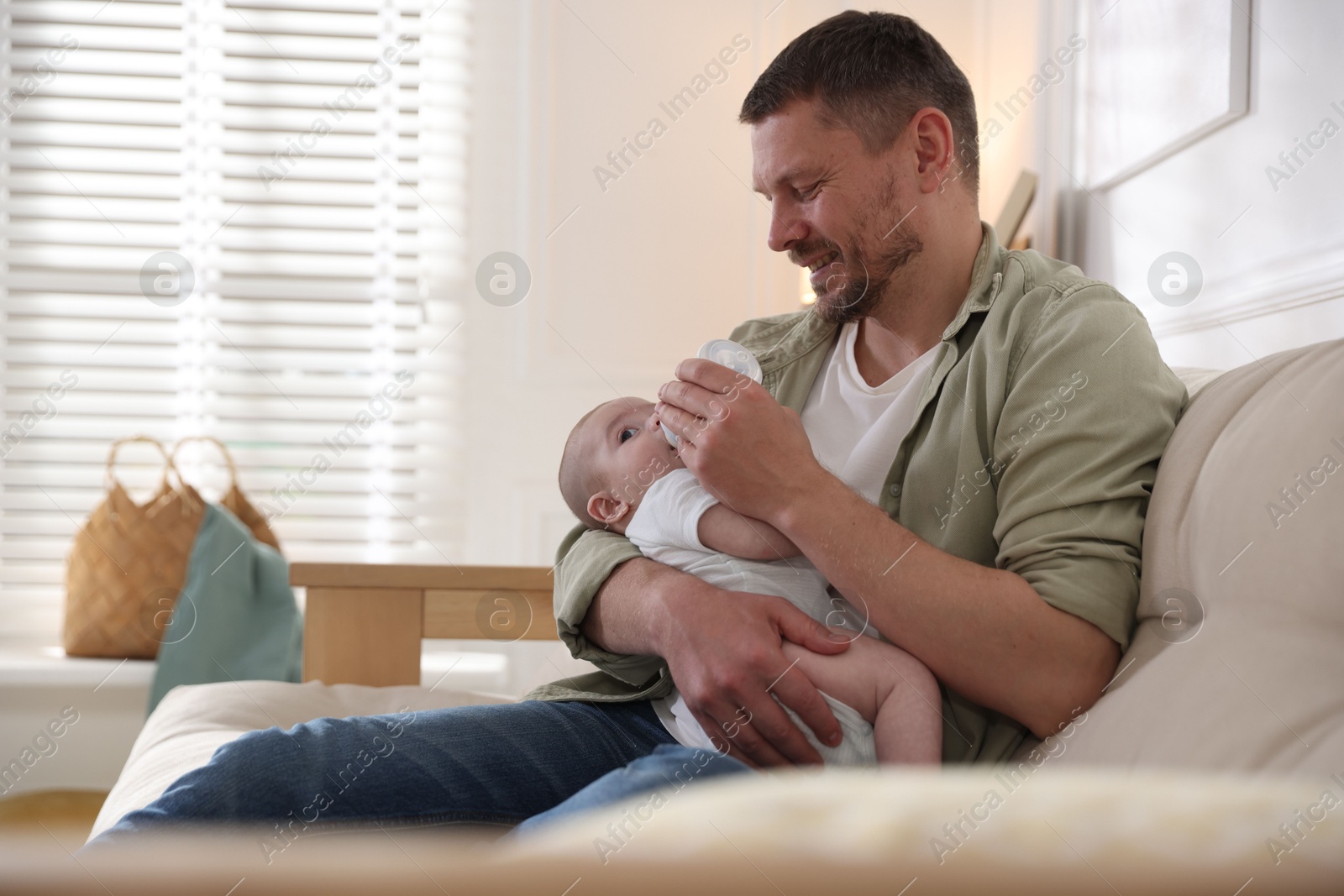Father feeding his little baby with bottle on sofa at home. Space for text Photo of Father feeding his little baby with bottle on sofa at home. Space for text