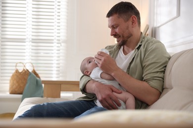Photo of Father feeding his little baby with bottle on sofa at home. Space for text