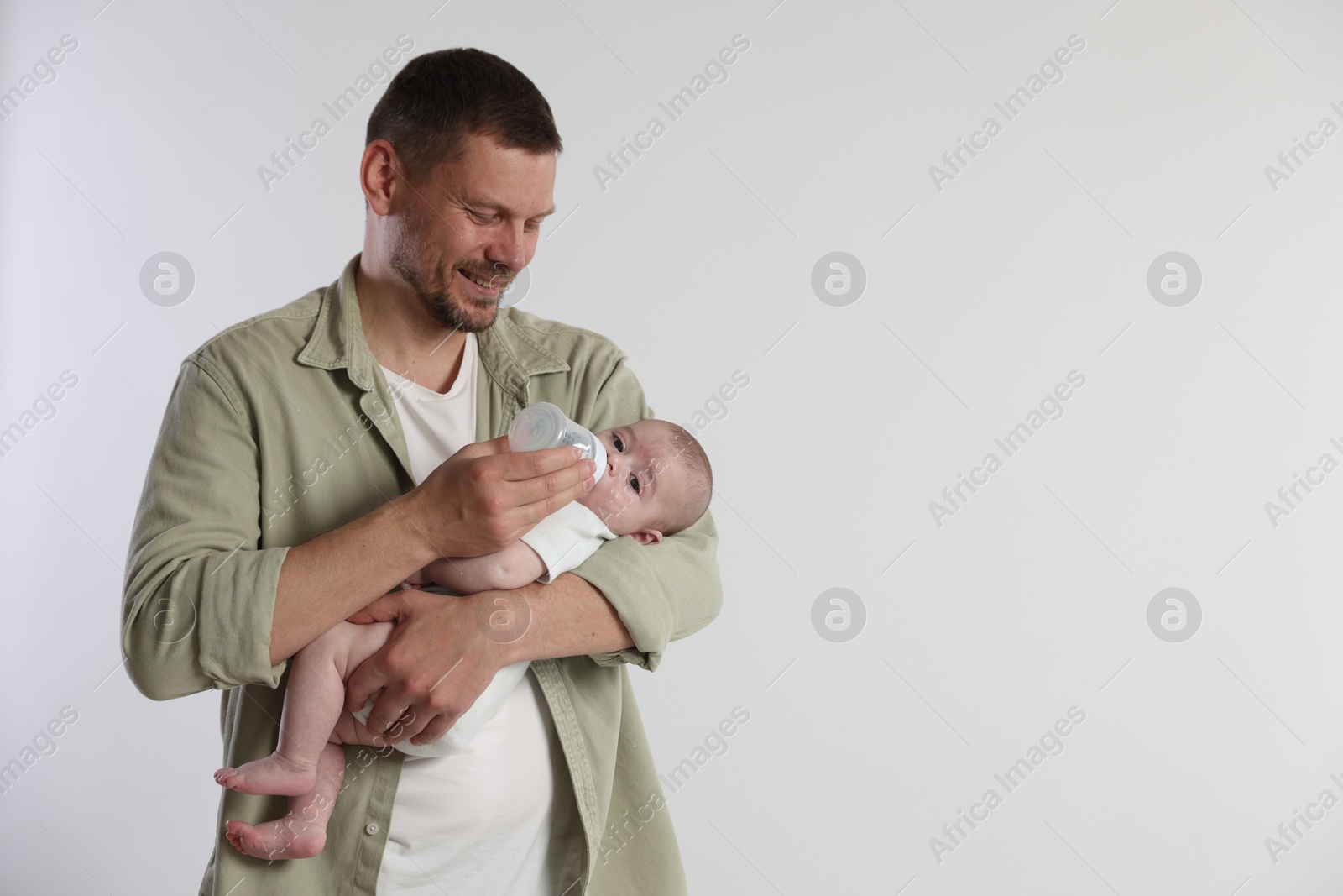 Father feeding his little baby with bottle on light background. Space for text Photo of Father feeding his little baby with bottle on light background. Space for text