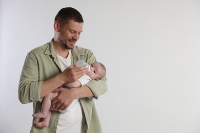 Photo of Father feeding his little baby with bottle on light background. Space for text