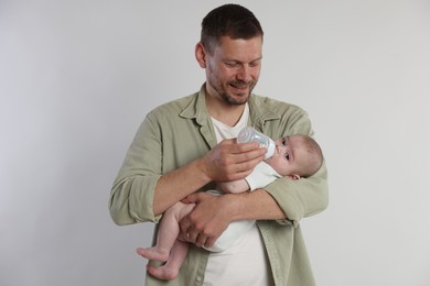 Photo of Father feeding his little baby with bottle on light background