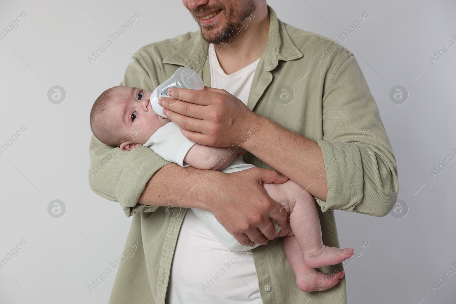 Father feeding his little baby with bottle on light background, closeup Photo of Father feeding his little baby with bottle on light background, closeup