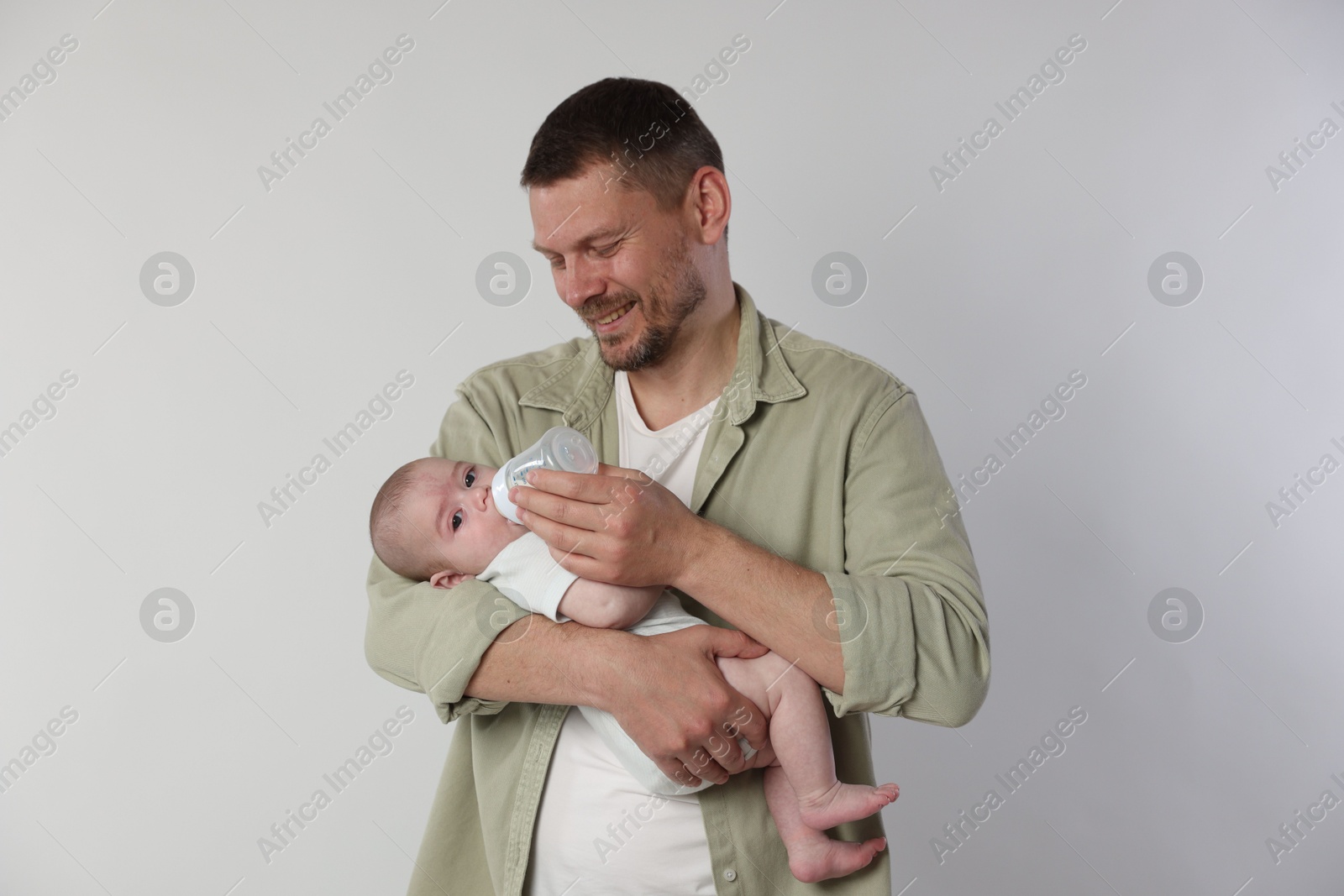 Father feeding his little baby with bottle on light background Photo of Father feeding his little baby with bottle on light background