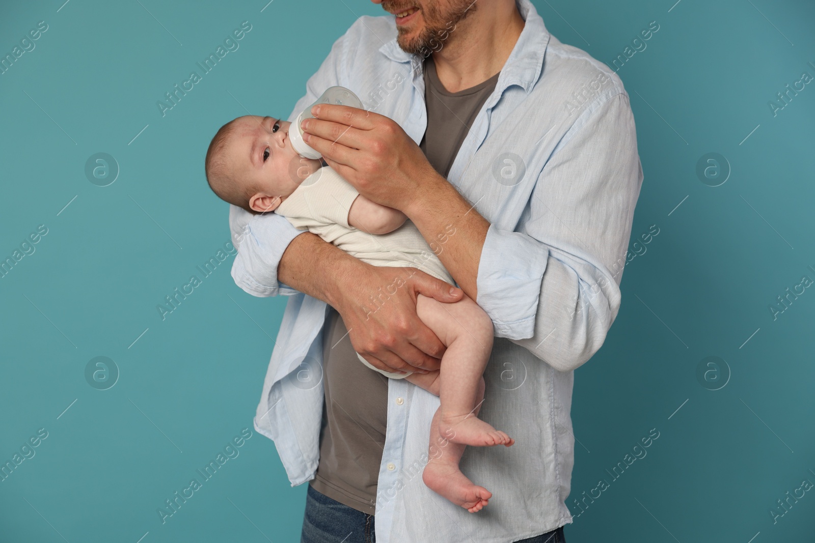 Father feeding his little baby with bottle on light blue background, closeup Photo of Father feeding his little baby with bottle on light blue background, closeup
