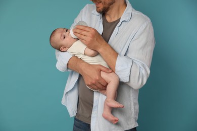 Photo of Father feeding his little baby with bottle on light blue background, closeup
