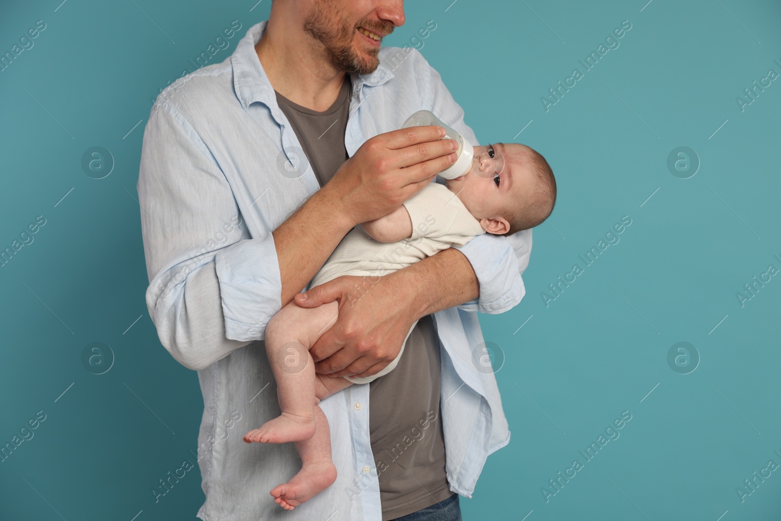 Father feeding his little baby with bottle on light blue background, closeup Photo of Father feeding his little baby with bottle on light blue background, closeup