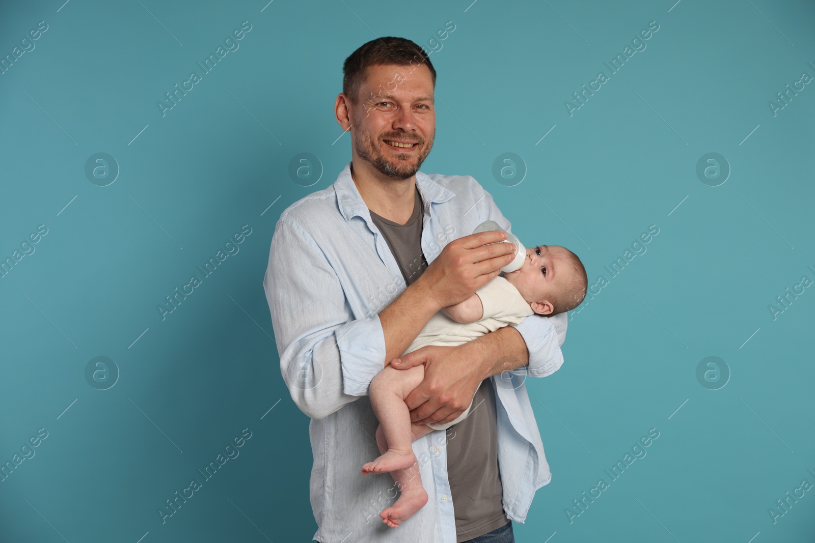 Father feeding his little baby with bottle on light blue background Photo of Father feeding his little baby with bottle on light blue background