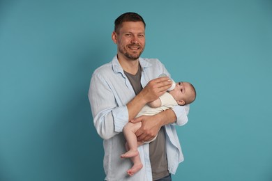 Photo of Father feeding his little baby with bottle on light blue background