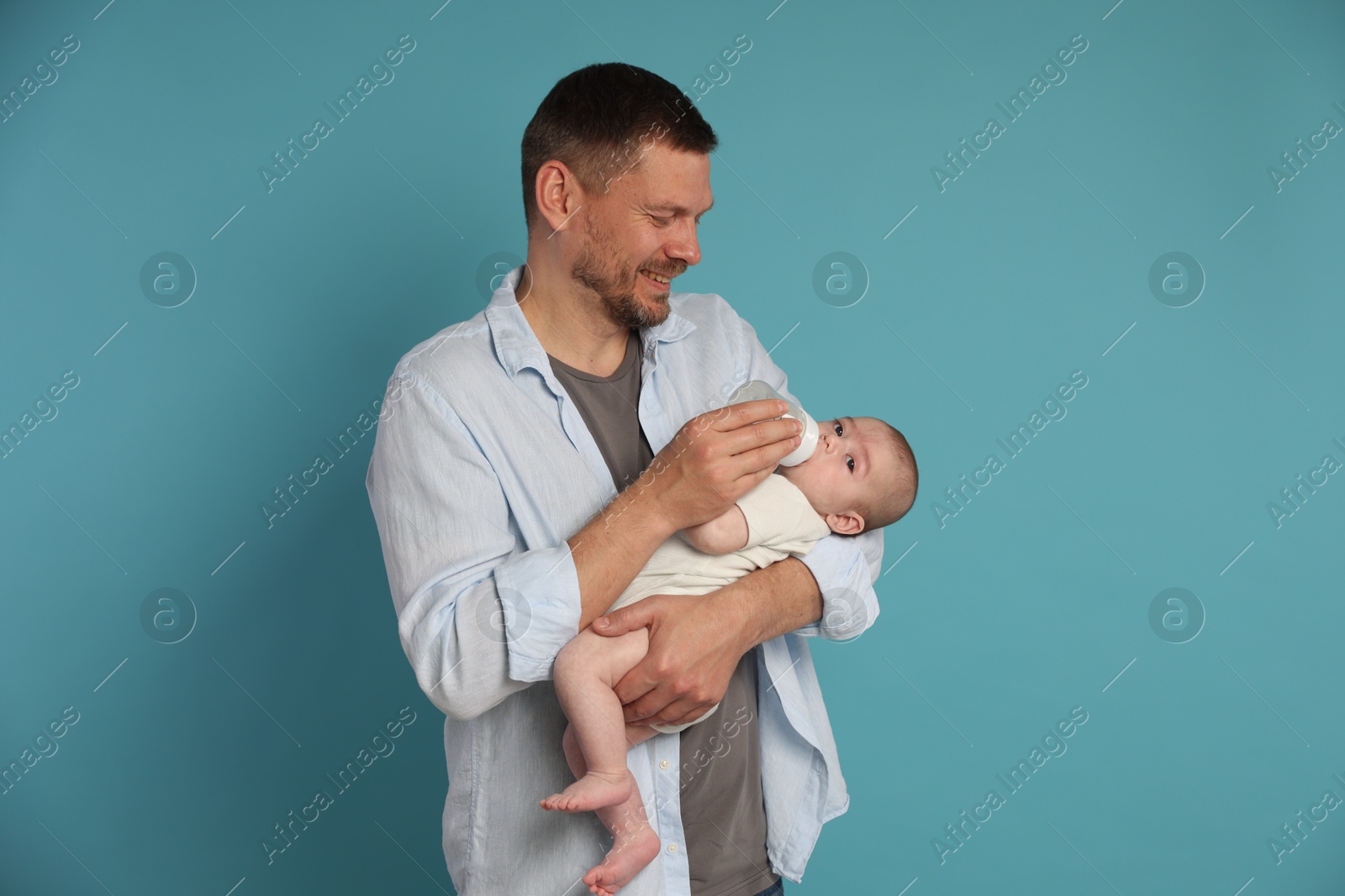 Photo of Father feeding his little baby with bottle on light blue background