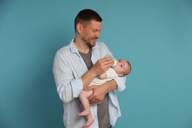 Photo of Father feeding his little baby with bottle on light blue background