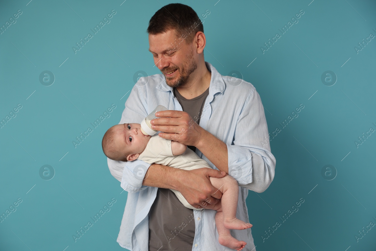 Father feeding his little baby with bottle on light blue background Photo of Father feeding his little baby with bottle on light blue background