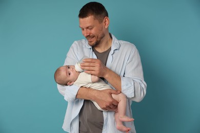 Photo of Father feeding his little baby with bottle on light blue background