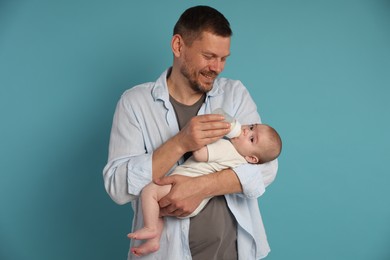 Photo of Father feeding his little baby with bottle on light blue background
