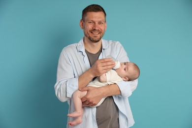 Photo of Father feeding his little baby with bottle on light blue background