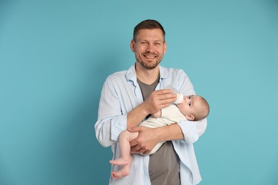 Photo of Father feeding his little baby with bottle on light blue background