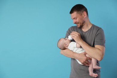 Photo of Father feeding his little baby with bottle on light blue background. Space for text