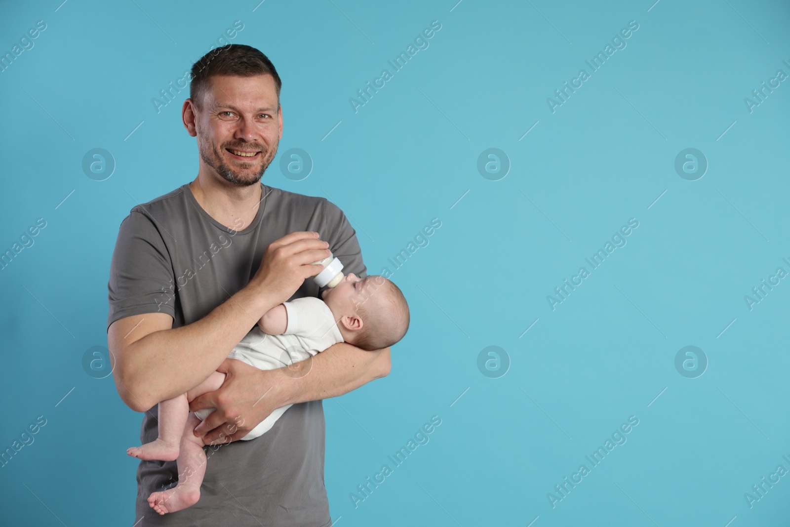Father feeding his little baby with bottle on light blue background. Space for text Photo of Father feeding his little baby with bottle on light blue background. Space for text