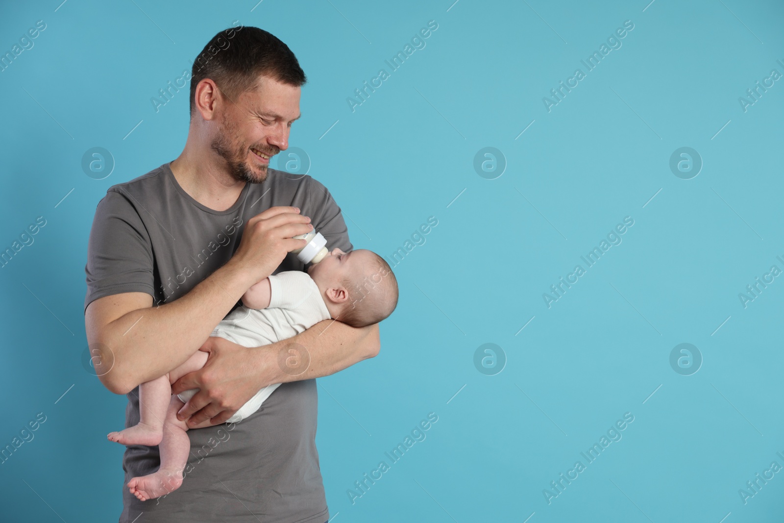 Father feeding his little baby with bottle on light blue background. Space for text Photo of Father feeding his little baby with bottle on light blue background. Space for text