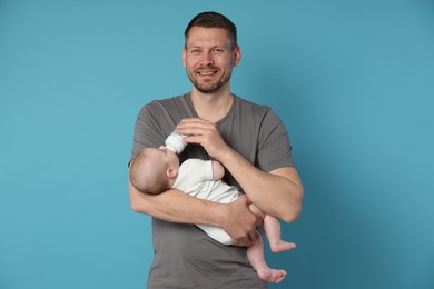 Photo of Father feeding his little baby with bottle on light blue background