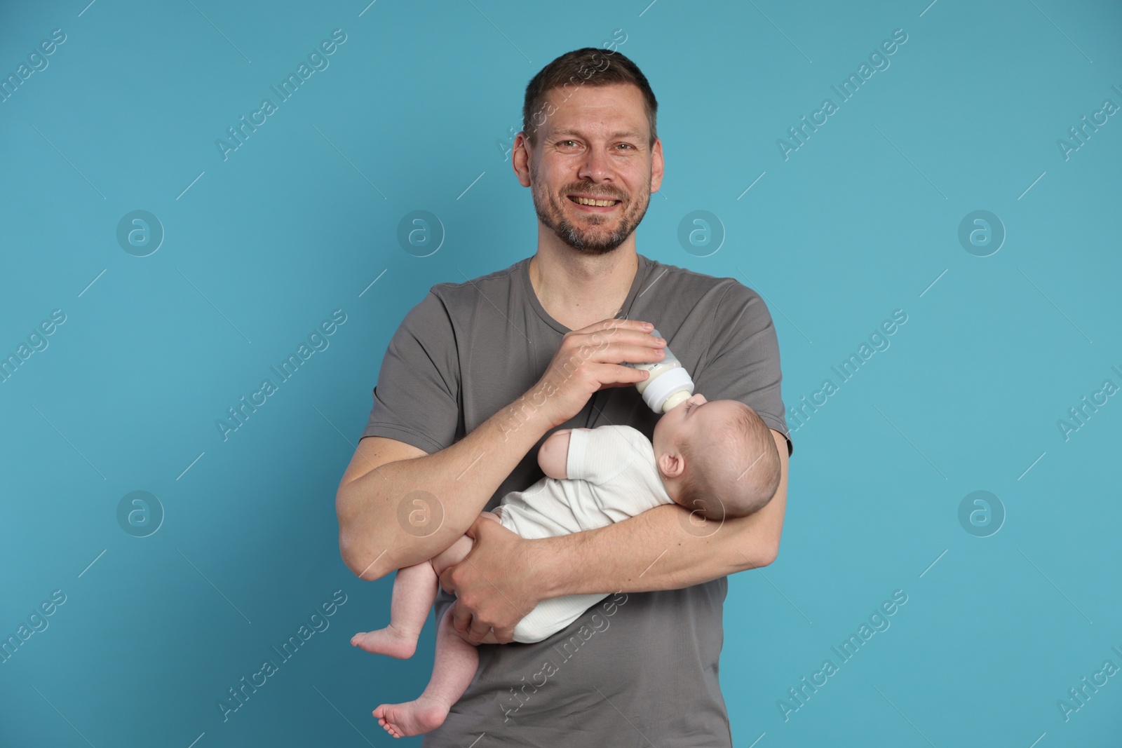 Father feeding his little baby with bottle on light blue background Photo of Father feeding his little baby with bottle on light blue background