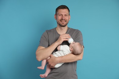 Photo of Father feeding his little baby with bottle on light blue background
