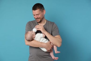 Photo of Father feeding his little baby with bottle on light blue background
