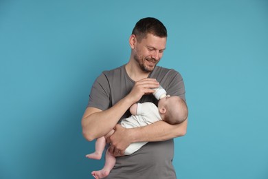 Photo of Father feeding his little baby with bottle on light blue background