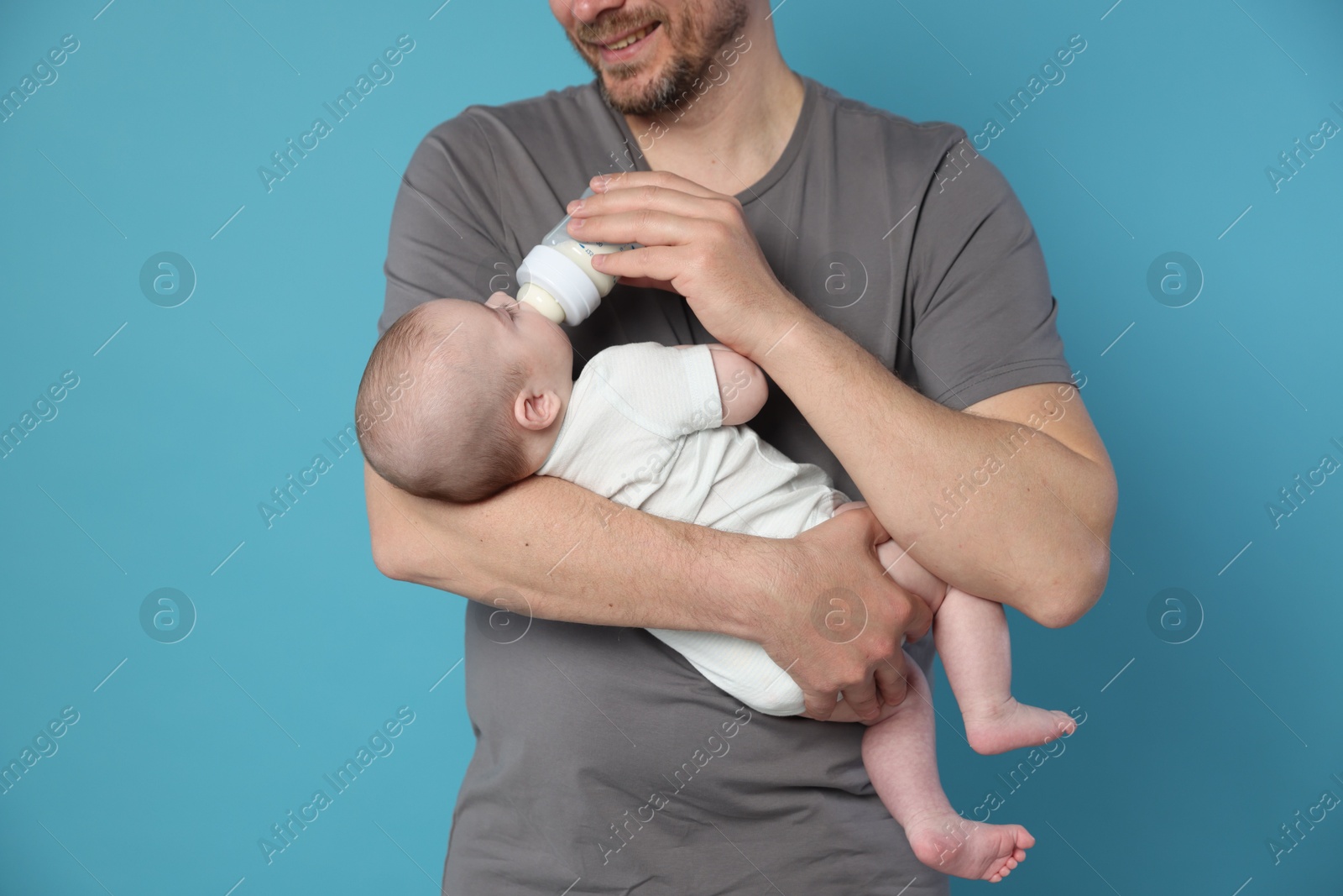 Father feeding his little baby with bottle on light blue background, closeup Photo of Father feeding his little baby with bottle on light blue background, closeup