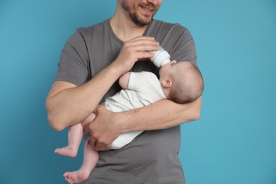 Photo of Father feeding his little baby with bottle on light blue background, closeup