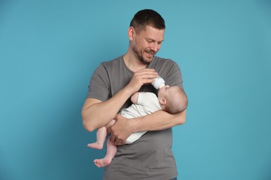 Photo of Father feeding his little baby with bottle on light blue background