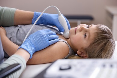 Photo of Sonographer conducting ultrasound examination of little girl's thyroid gland in clinic, closeup