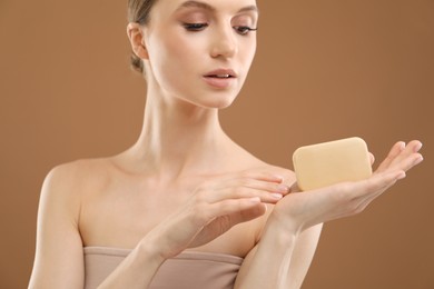 Photo of Beautiful woman with soap bar on brown background, closeup