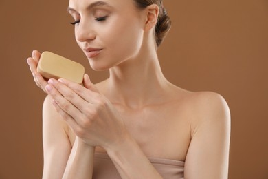 Photo of Beautiful woman with soap bar on brown background, closeup