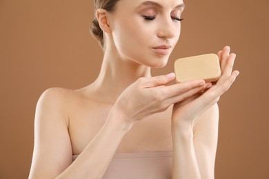 Photo of Beautiful woman with soap bar on brown background, closeup