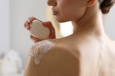 Photo of Woman washing body with soap bar indoors, closeup