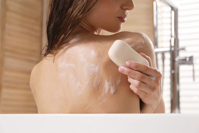 Photo of Woman washing body with soap bar in bathroom, closeup