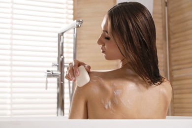 Photo of Woman washing body with soap bar in bathroom