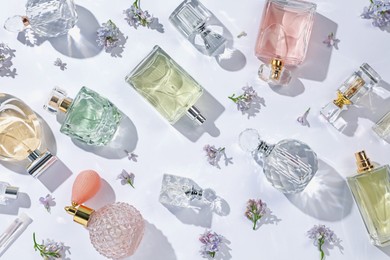 Photo of Luxury perfumes and beautiful lilac flowers on white background, flat lay