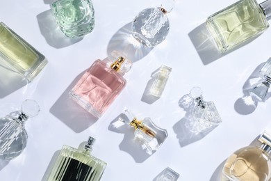 Photo of Luxury perfumes and beautiful lilac flowers on white background, flat lay