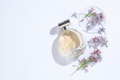 Photo of Bottle of perfume and beautiful lilac flowers on white background, flat lay. Space for text