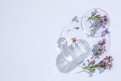 Photo of Bottle of perfume and beautiful lilac flowers on white background, flat lay. Space for text
