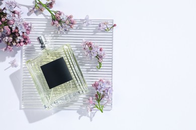 Photo of Bottle of perfume and beautiful lilac flowers on white background, flat lay. Space for text