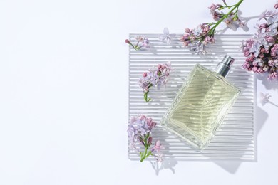 Photo of Bottle of perfume and beautiful lilac flowers on white background, flat lay. Space for text
