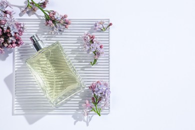 Photo of Bottle of perfume and beautiful lilac flowers on white background, flat lay. Space for text
