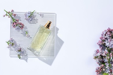 Photo of Bottle of perfume and beautiful lilac flowers on white background, flat lay. Space for text