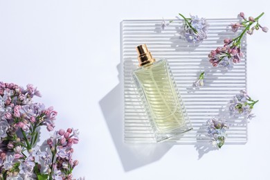 Photo of Bottle of perfume and beautiful lilac flowers on white background, flat lay
