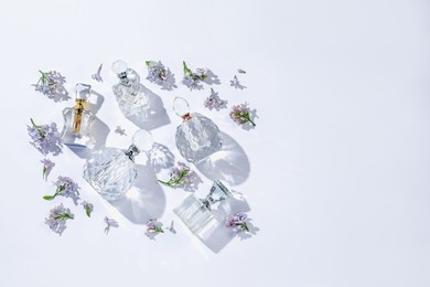 Photo of Luxury perfumes and beautiful lilac flowers on white background, flat lay. Space for text