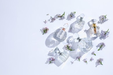 Photo of Luxury perfumes and beautiful lilac flowers on white background, flat lay. Space for text