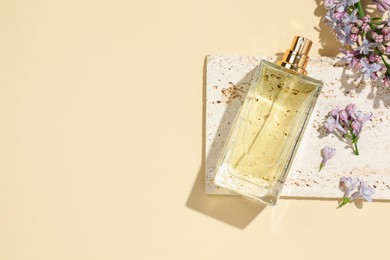 Photo of Bottle of perfume and beautiful lilac flowers on pale yellow background, flat lay. Space for text