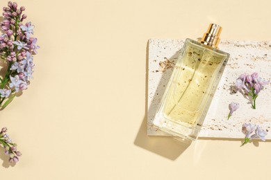 Photo of Bottle of perfume and beautiful lilac flowers on pale yellow background, flat lay. Space for text